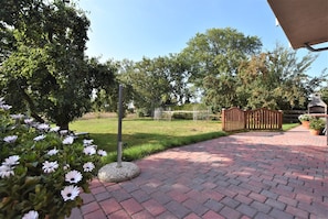 A paved pathway leading to a gated area with a tree-lined backdrop.