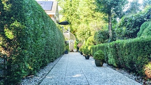 A pathway lined with neatly trimmed hedges and potted plants, leading towards a building with a staircase. - Quaint Apartment in Oostkapelle Zealand With Terrace (Oostkapelle)