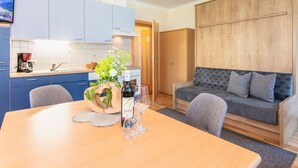 A modern kitchen with blue cabinets, a wooden dining table with a vase of flowers and wine glasses, and a grey sofa with patterned cushions. - Elegant Apartment in Saalbach-hinterglemm Near Ski Bus (Saalbach-Hinterglemm)