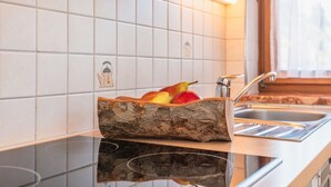 A kitchen with white tiles, a wooden fruit basket on the counter, and a window with curtains. - Elegant Apartment in Saalbach-hinterglemm Near Ski Bus (Saalbach-Hinterglemm)