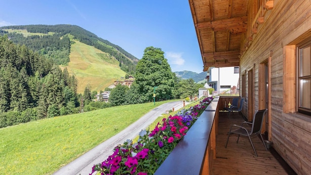 A wooden building with a balcony overlooking a road with colorful flowers and a mountainous landscape. - Elegant Apartment in Saalbach-hinterglemm Near Ski Bus (Saalbach-Hinterglemm)