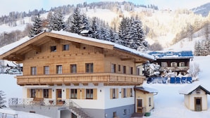 A multi-story wooden chalet with a balcony, surrounded by snow-covered trees and mountains. - Elegant Apartment in Saalbach-hinterglemm Near Ski Bus (Saalbach-Hinterglemm)