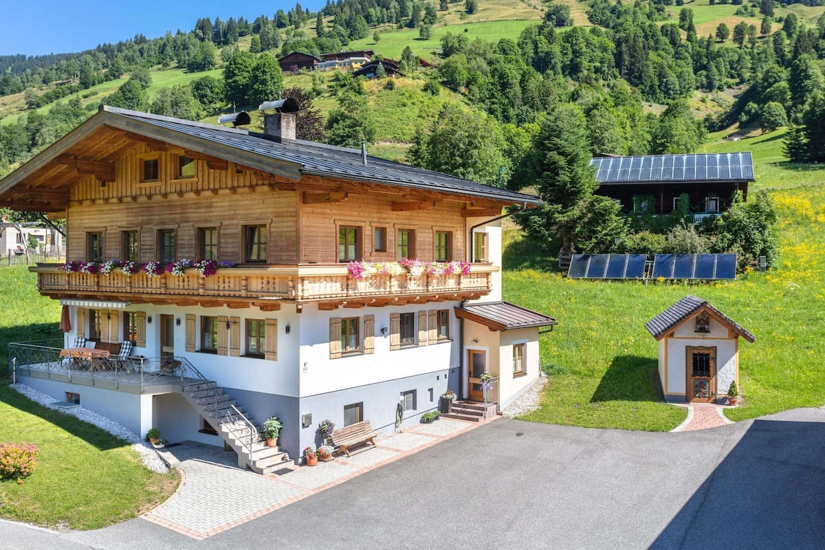 A two-story chalet with a balcony, a small attached structure, and solar panels in the background.