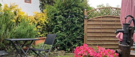 A garden with a wooden gate, a metal table and chair, and a flower pot with pink flowers.