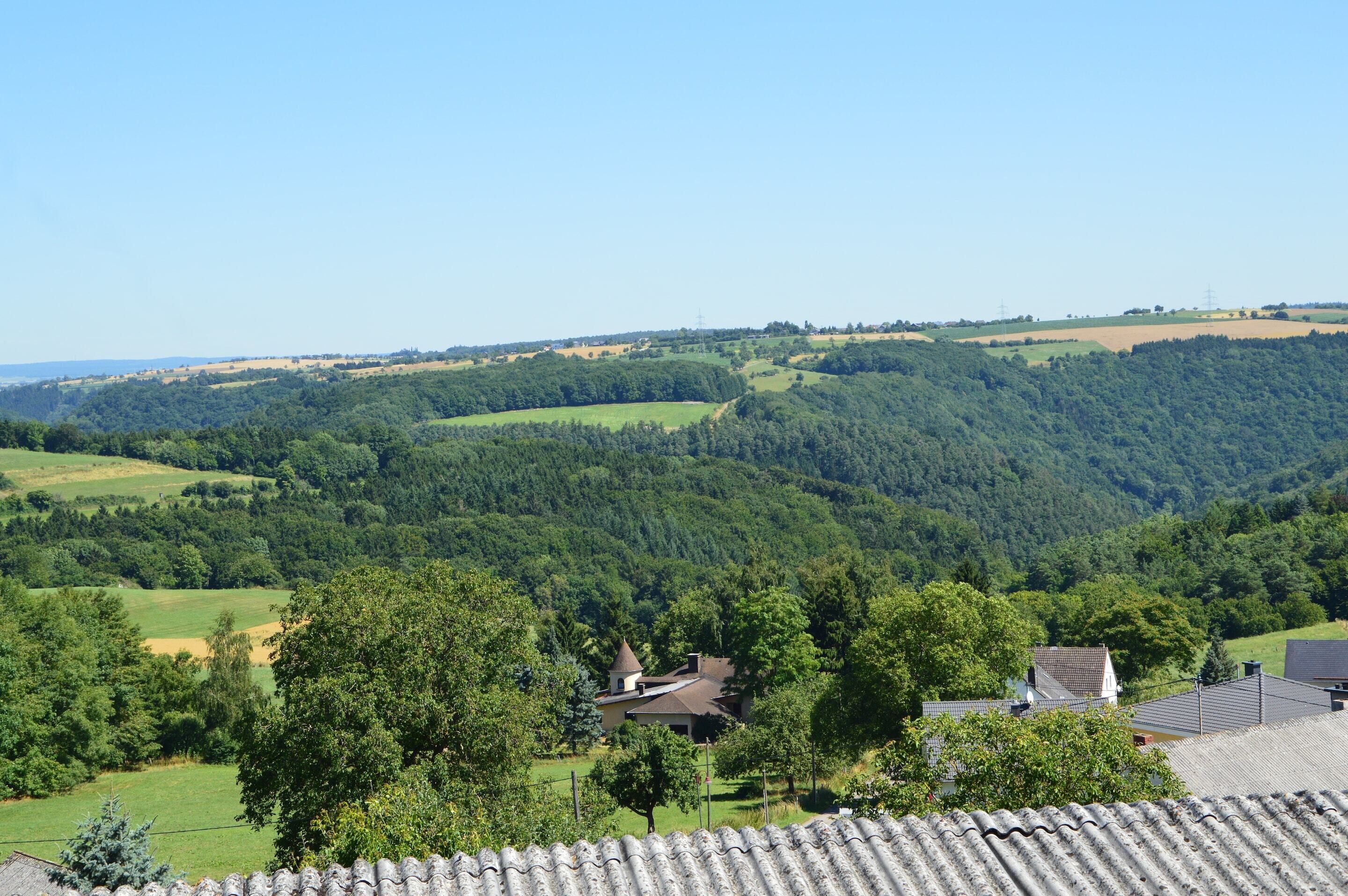 A rural landscape with rolling hills, a small house with a conical roof, and a clear blue sky.