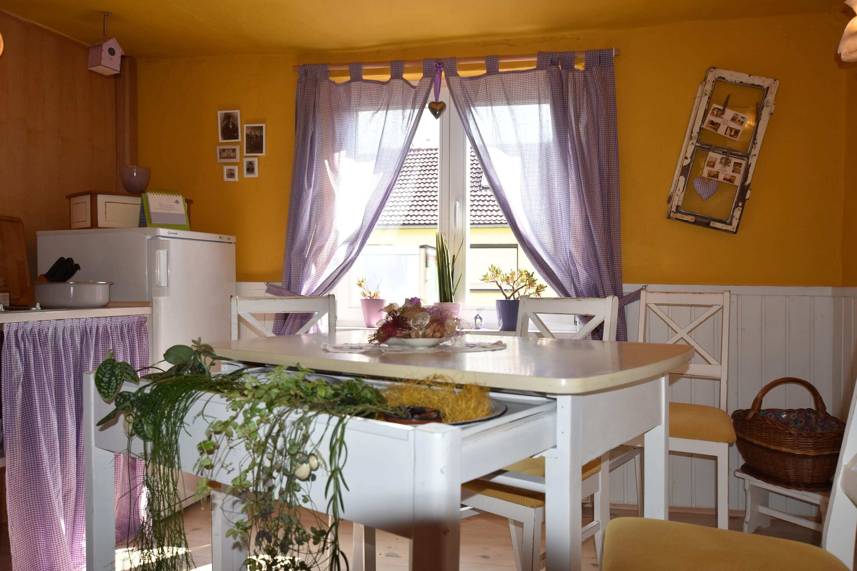 A dining area with a white table, purple curtains, and a window with a view.