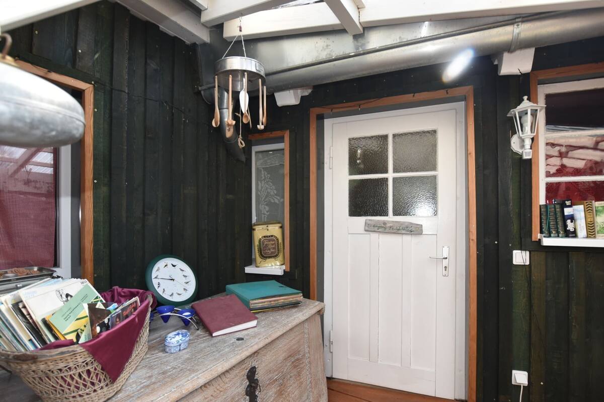 A rustic room with a wooden desk, a white door, a window with frosted glass, and a shelf with books and a canister.