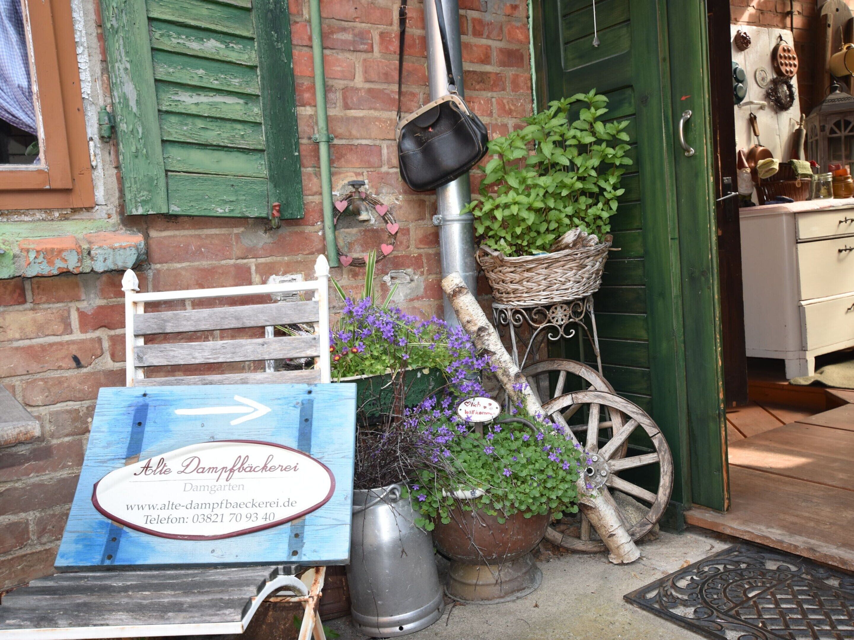 A rustic outdoor seating area with a wooden bench, a signboard, a wicker basket, and potted plants.