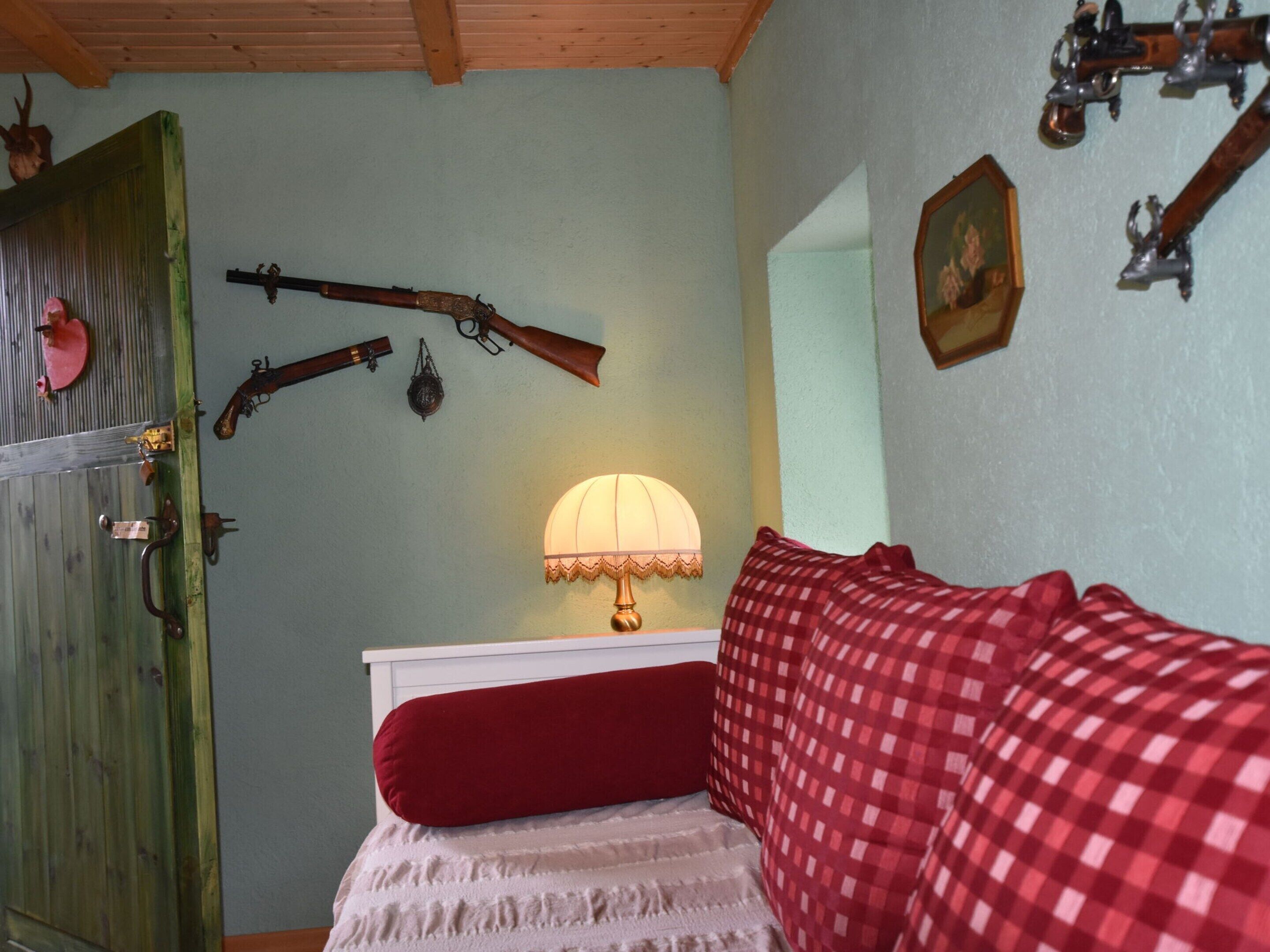 A bedroom with a bed, a lamp, and wall-mounted firearms.