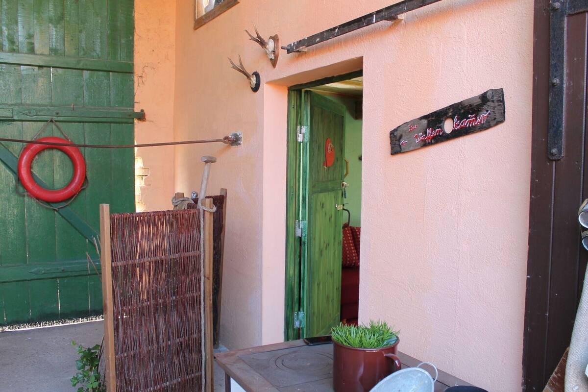 A rustic outdoor entrance with a green door, a wooden fence, and a sign indicating a restaurant.