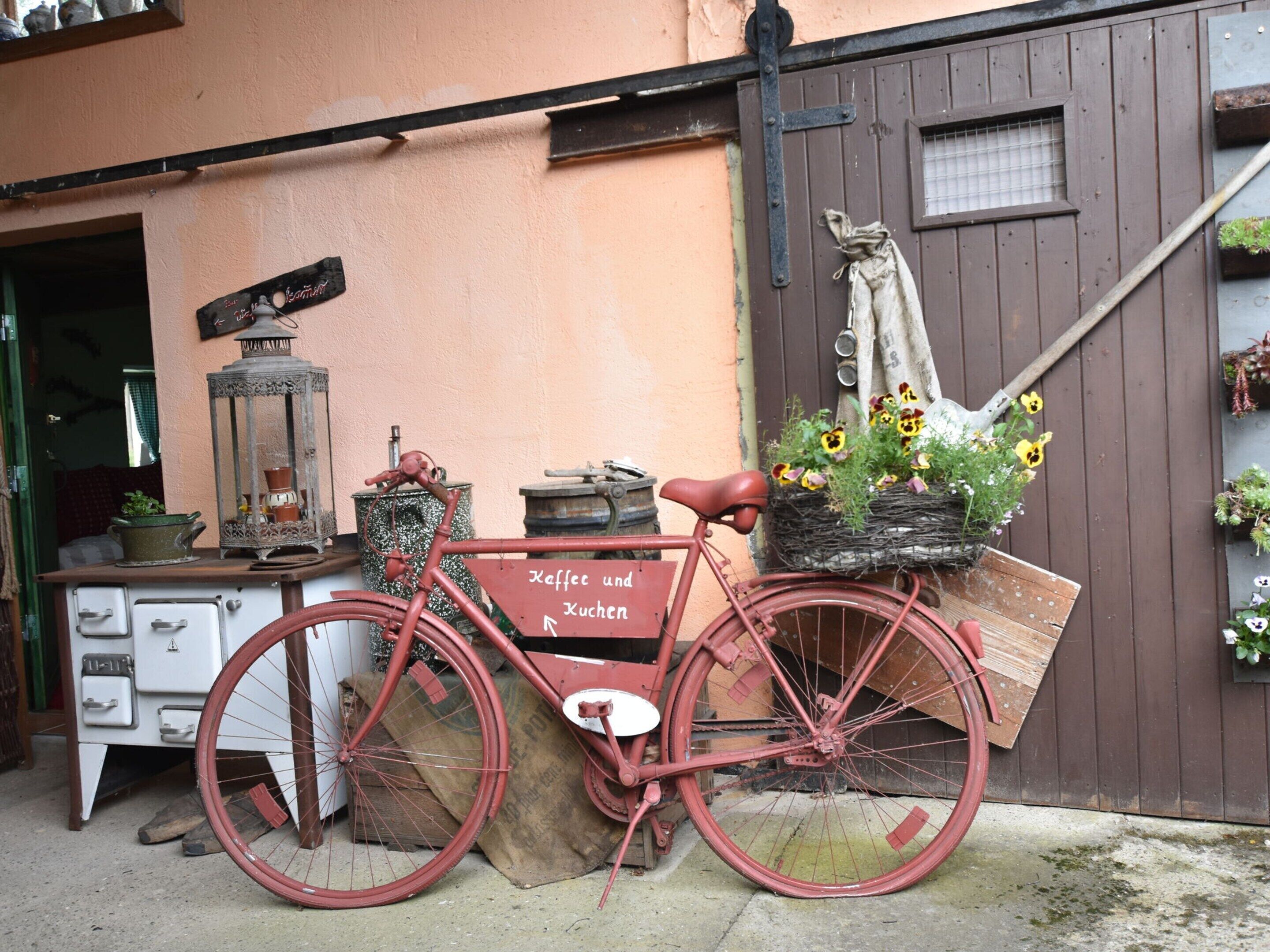 A vintage bicycle with a basket of flowers parked outside a building with a wooden door and a window.