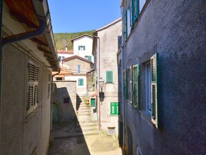 Una calle estrecha con edificios de piedra, contraventanas verdes y un cielo despejado.