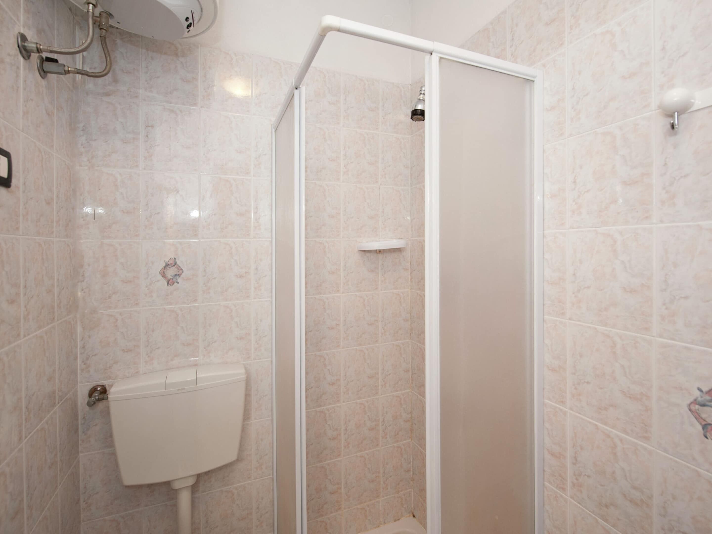 Une douche avec une porte en verre, des toilettes et un robinet fixé au mur.