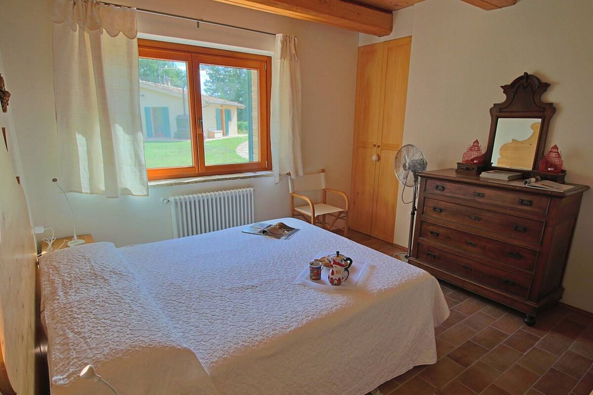 Ein Schlafzimmer mit einem Bett, einem Schminktisch, einem Stuhl, einem Heizkörper und einem Fenster mit Vorhängen.