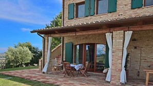 Una casa a due piani con facciata in mattoni, persiane verdi e un patio coperto con mobili da esterno.