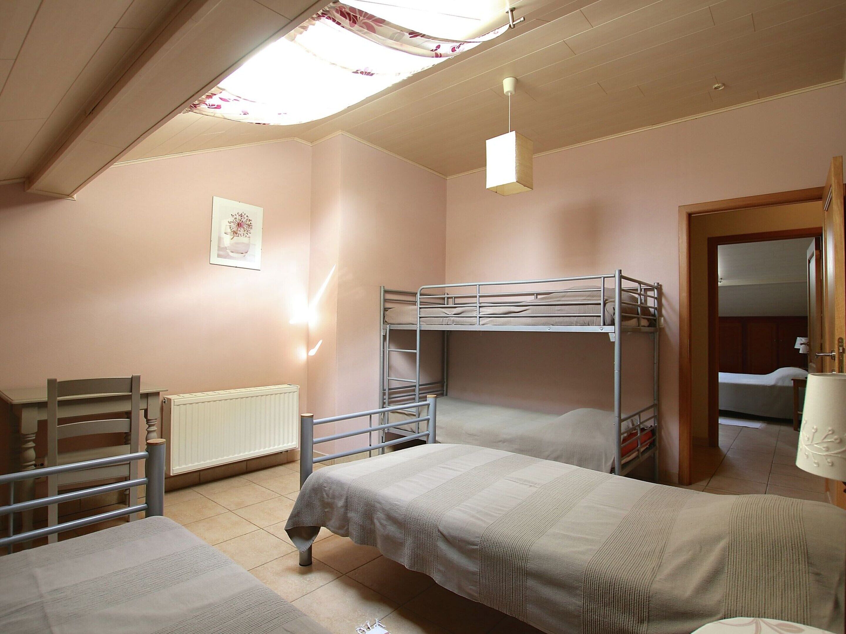 A dormitory room with bunk beds, a desk, a chair, a radiator, and a door leading to another room.