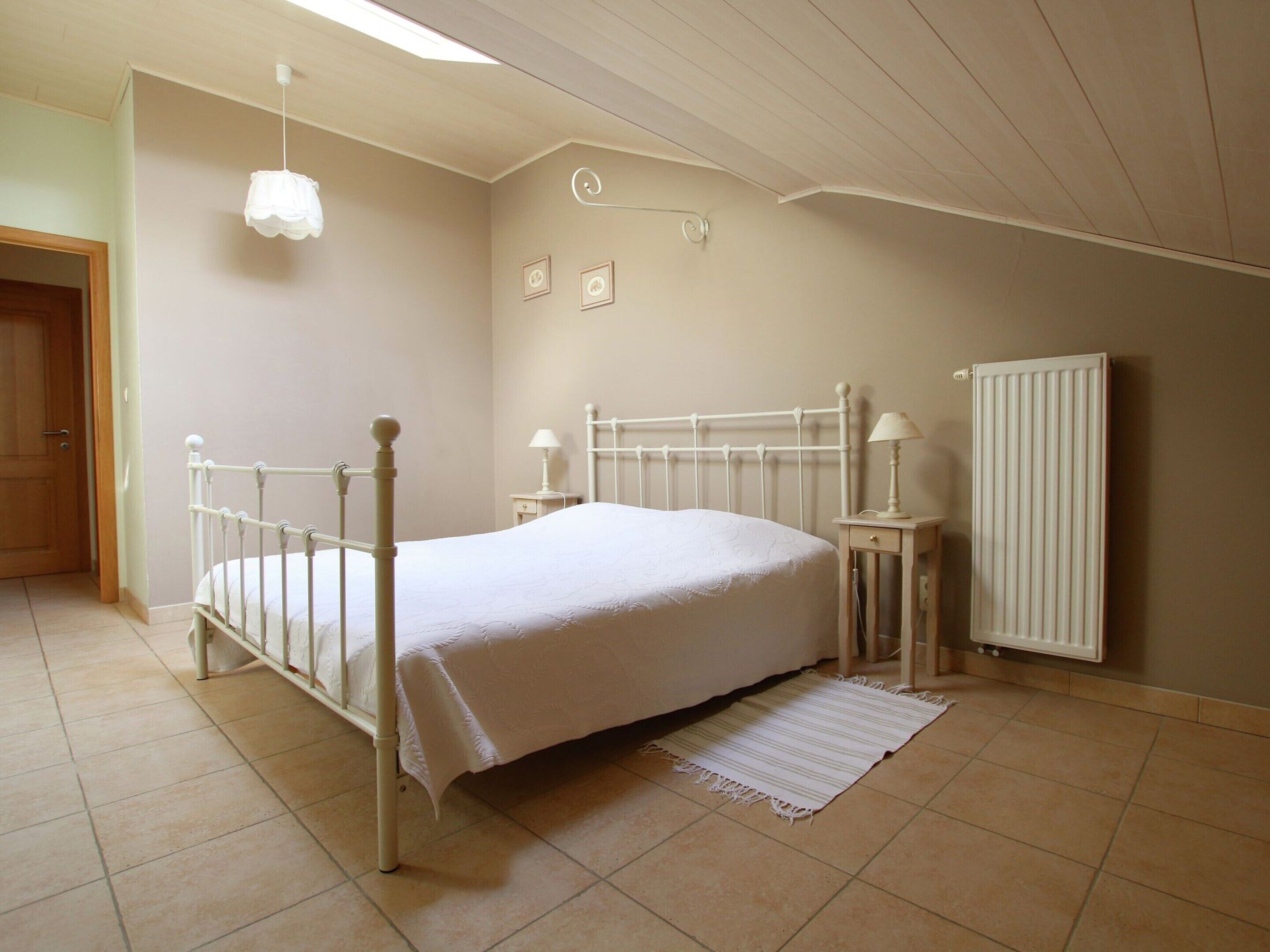 Un dormitorio con una cama individual, una mesita de noche con lámpara, un radiador y una lámpara colgante.