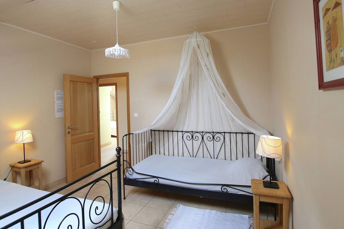 A bedroom with a canopy bed, a wooden door, a bedside table with a lamp, and a small table with a lamp.