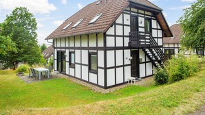 A traditional half-timbered house with a sloped roof, a staircase leading to the upper floor, and a small outdoor seating area.
