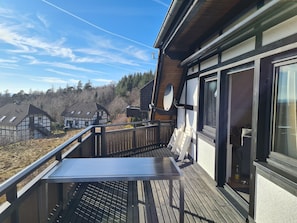 Une terrasse en bois avec une table et des chaises, donnant sur un quartier résidentiel avec des maisons traditionnelles.