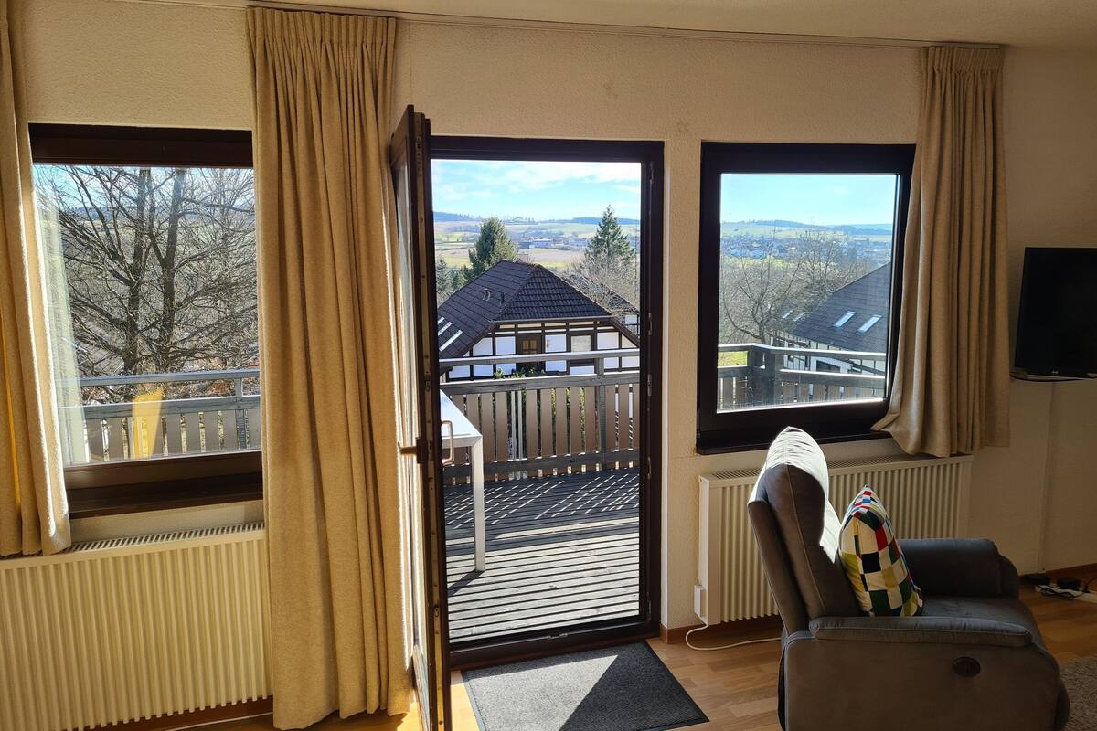 A living room with a view of a house and trees through open doors.