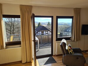 A living room with a view of a house and trees through open doors.