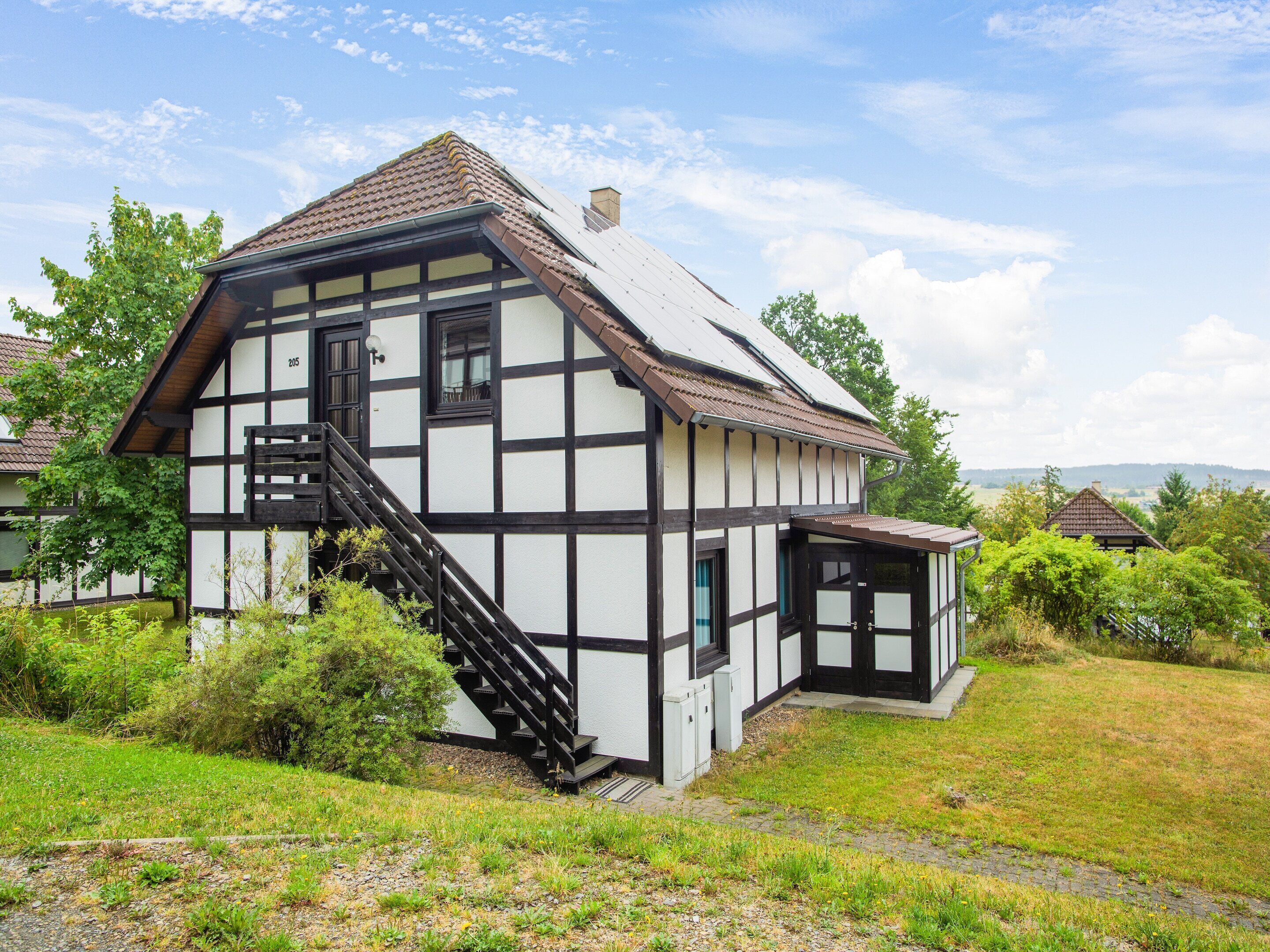 A traditional half-timbered house with a steep staircase, a small porch, and a view of the surrounding landscape.