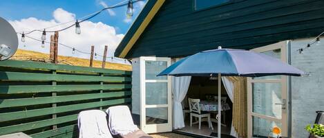 A patio with two lounge chairs, a table with drinks, and a blue umbrella.