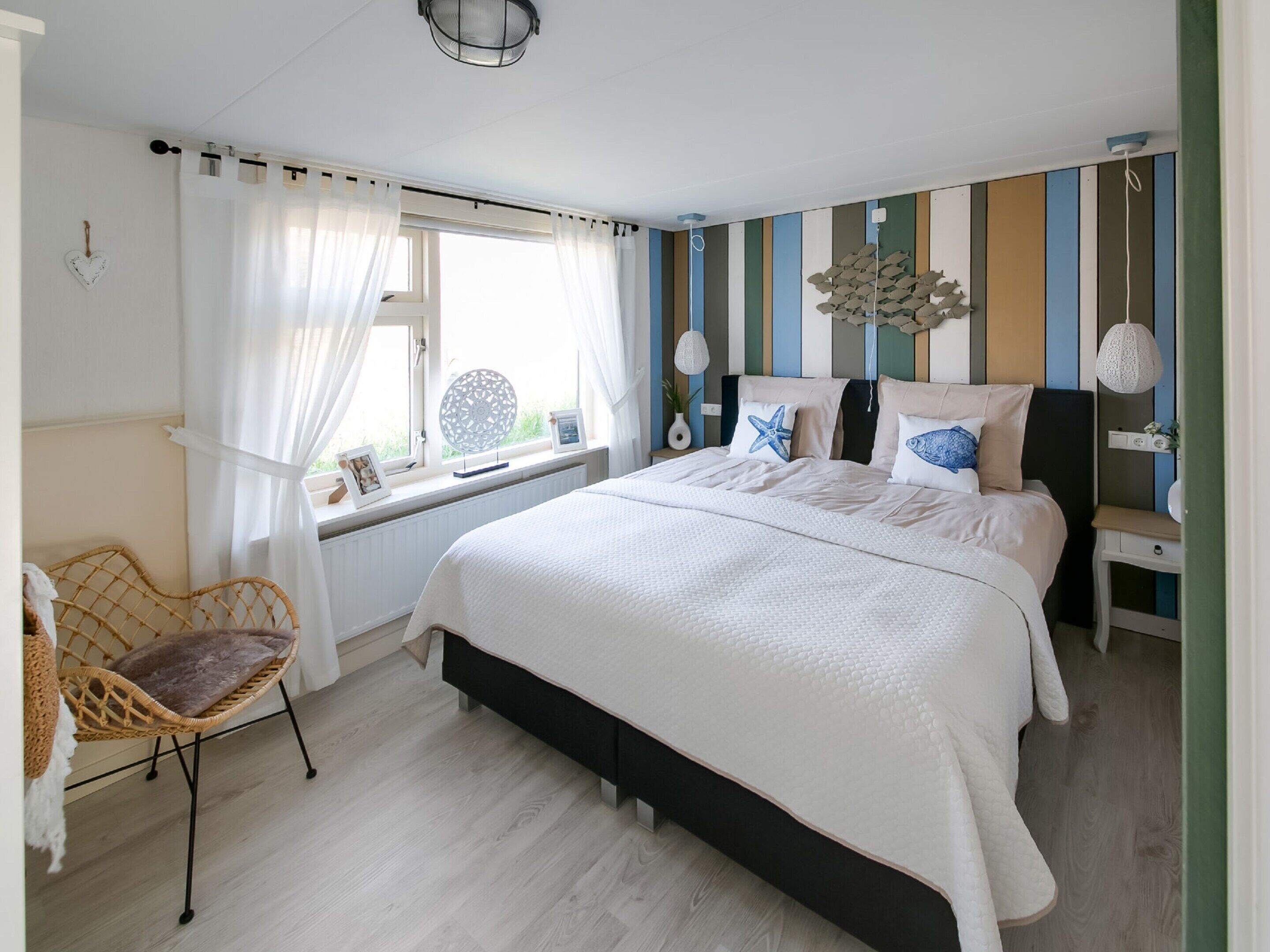 Ein Schlafzimmer mit einem großen Bett, einem Sessel, einem Nachttisch und einem Fenster mit Vorhängen.