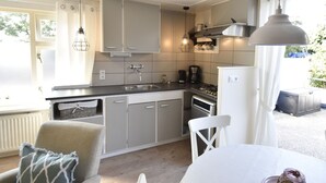 A compact kitchen with grey cabinets, a sink, a stove, and a white refrigerator. There is a hanging light fixture above the counter. - Beautiful Apartment in Callantsoog Near Beach (t Zand)