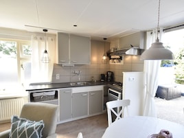 A compact kitchen with grey cabinets, a sink, a stove, and a white refrigerator. There is a hanging light fixture above the counter.