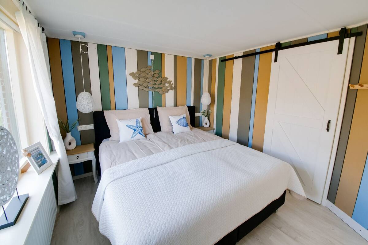 A bedroom with a bed, bedside tables, a dresser, and a striped wall.