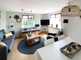 A living room with a sofa, coffee table, and TV. There is a window with blinds, a lamp, and a decorative item on the wall.