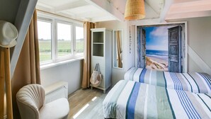 A bedroom with a bed, a chair, a wardrobe, a window with curtains, and a beach view painting. - Beautiful Apartment in Callantsoog Near Beach (t Zand)