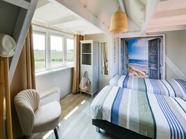 A bedroom with a bed, a chair, a wardrobe, a window with curtains, and a beach view painting.