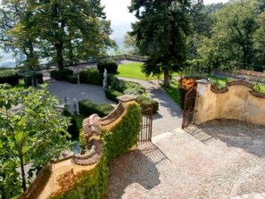 A landscaped garden with a curved wall, a gate, and a pathway leading to a body of water. - Charming Elegant Castle Flat With Large Garden (Rocca Grimalda)