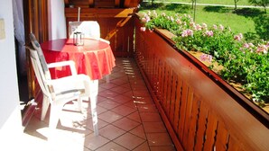 A balcony with a red table and white chairs, overlooking a garden with pink flowers and a green landscape. - Comfortable Holiday Home in a Beautiful Location (Hofstetten)