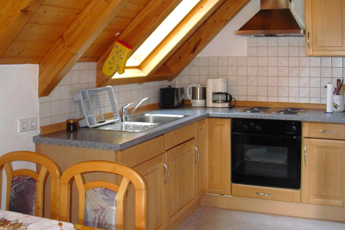 A kitchen with wooden cabinets, a sink, a stove, and a window with a hanging pot holder.