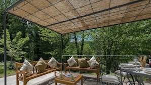 An outdoor patio with wooden furniture, a table set for dining, and a covered area with a bamboo roof. - Restful Holiday Home in Reggello With Swimming Pool (Reggello)