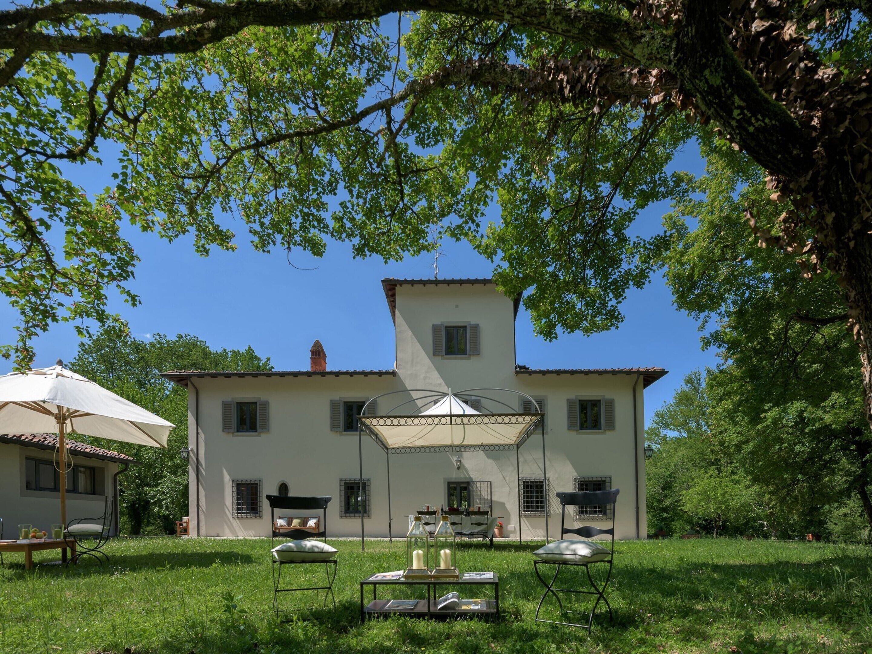 Una grande casa con un'area salotto esterna coperta, un tavolino con libri e candele, e una poltrona.