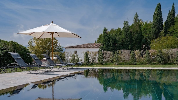 A swimming pool with lounge chairs and an umbrella, surrounded by greenery and a building. - Restful Holiday Home in Reggello With Swimming Pool (Reggello)