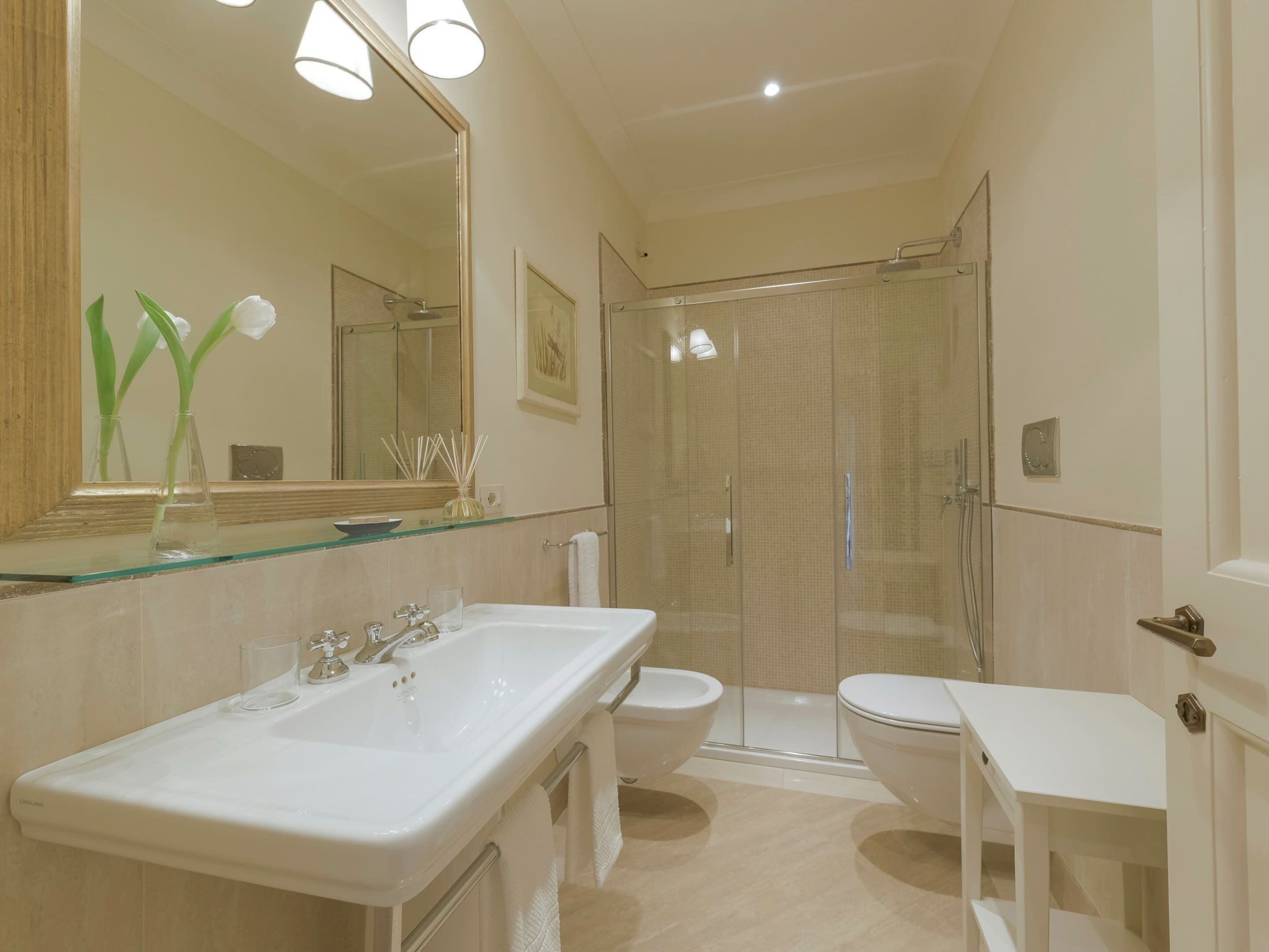 Une salle de bain moderne avec un grand miroir, deux lavabos, des toilettes et une douche à parois de verre.