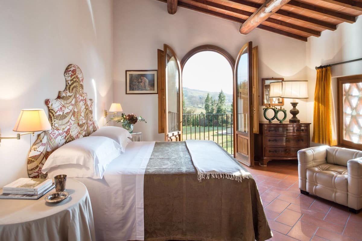 Une chambre à coucher avec un lit, une table de chevet avec une lampe, une chaise et une vue sur l’extérieur.