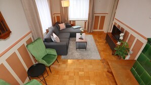 A modern living room with a sectional sofa, green armchairs, a small coffee table, and a TV on a stand. - Cozy Apartment in Schwenningen With Garden (Villingen-Schwenningen)