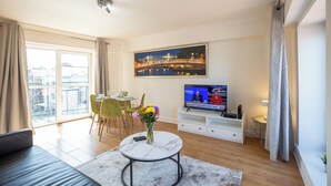 Un salon moderne comprenant un canapé, une table basse ronde, un téléviseur et un coin repas avec des chaises et une table.