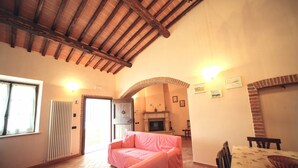 A cozy living room with a pink sofa, a fireplace, and a dining area with a table and chairs. - Lovely Farmhouse in Asciano With Swimming Pool (Asciano)