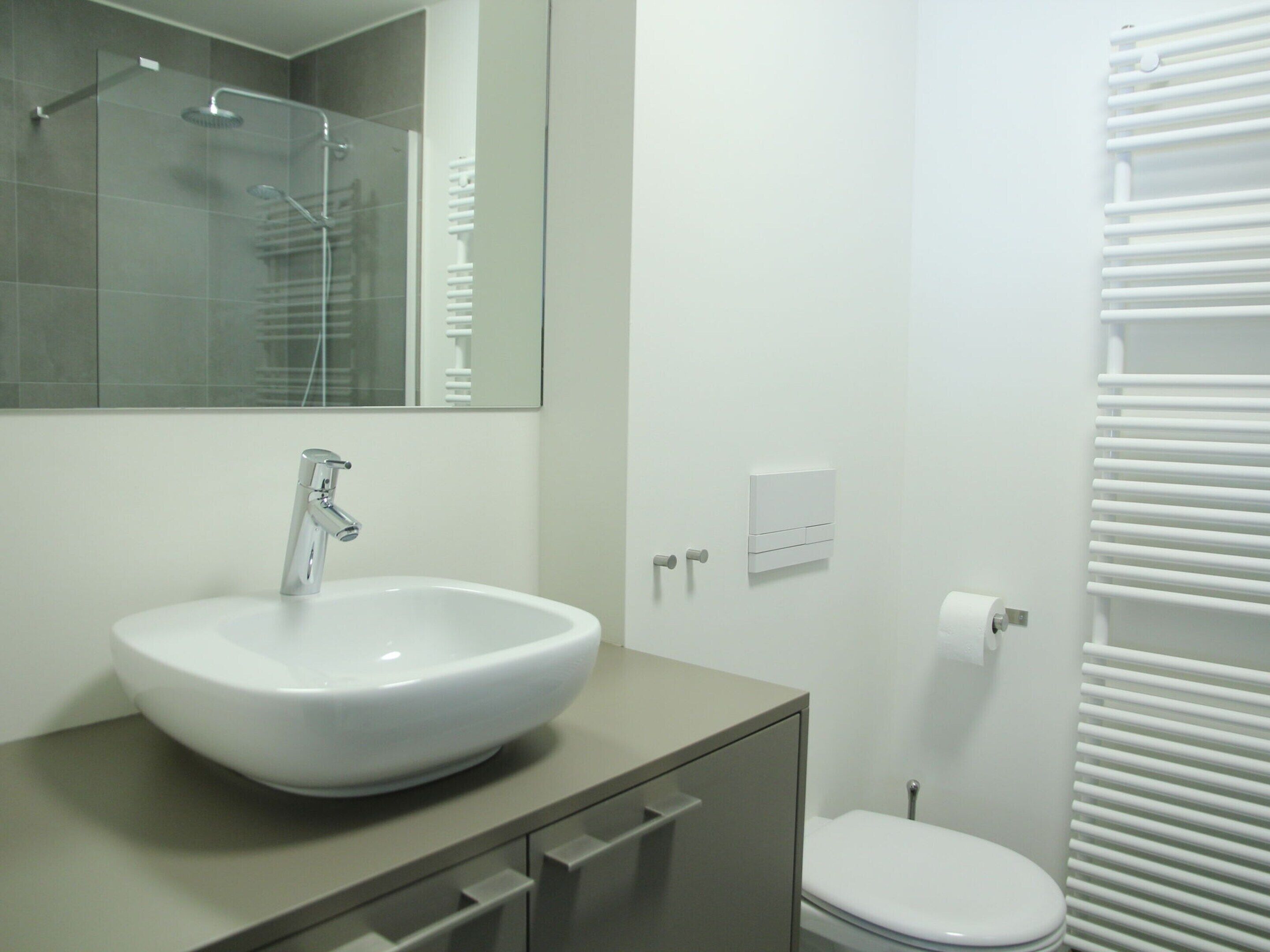 Une salle de bain moderne avec un lavabo, un miroir et des toilettes, le tout de couleur blanche.