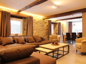 A cozy living room with a stone wall, a sofa, a coffee table, and a dining area with chairs and a table. - Beautiful Holiday Home in Ondenval With Private Terrace (Waimes)
