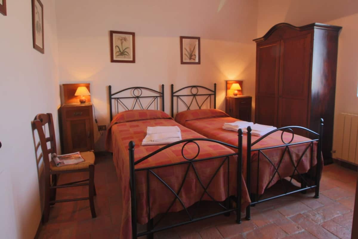 A bedroom with two beds, a wooden wardrobe, a chair, and two wall-mounted lamps.