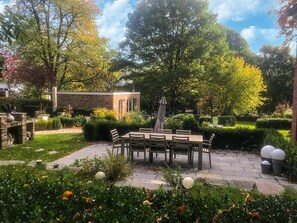 Una zona patio con tavolo e sedie, circondata da siepi e alberi ben curati.